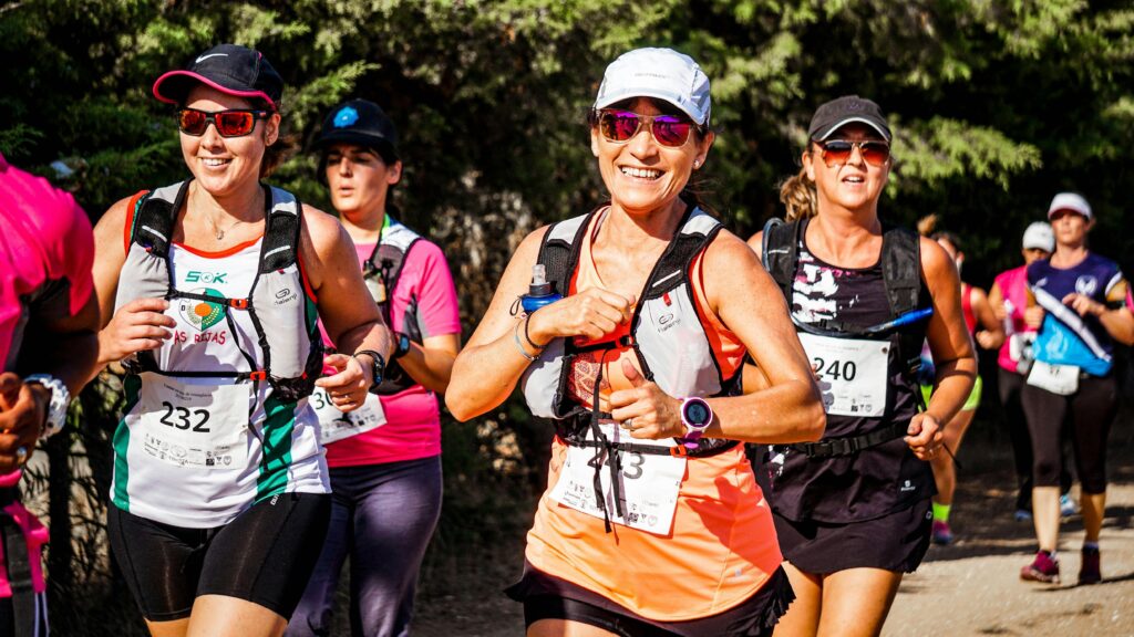 pexels-photo-1571939-1571939 A group of smiling women participating in an outdoor marathon run with race numbers.